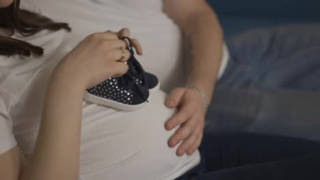 Unrecognizable-pregnant-woman-and-her-husband-holding-baby-shoes-on-belly