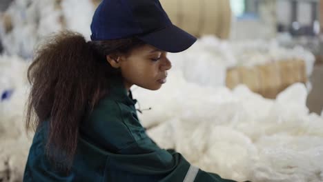 An-African-American-woman-in-a-special-uniform-sorts-polyethylene-at-a-waste-recycling-plant.-Processing-of-raw-materials,-recycling.-Pollution-control