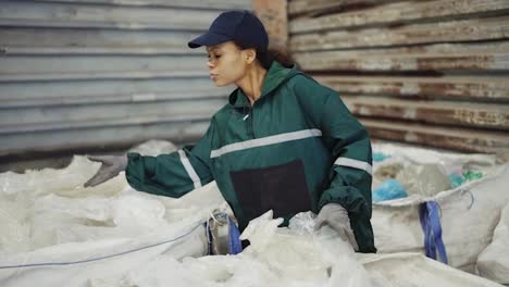 and-African-American-woman-in-a-special-uniform-sorts-polyethylene-at-a-waste-recycling-plant.-Processing-of-raw-materials