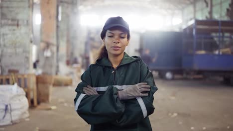 portrait-of-an-African-American-woman-in-a-special-green-uniform-against-the-background-of-the-interior-of-a-waste-processing-plant.-Processing-of-raw-materials,-recycling.-Pollution-control