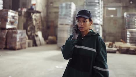 an-African-American-woman-in-a-special-green-uniform-speaks-on-the-phone-at-a-waste-processing-plant.-Factory-background.-Processing-of-raw-materials,-recycling.-Pollution-control