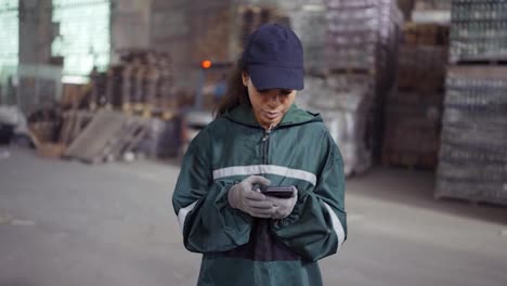 and-african-american-woman-in-a-special-green-uniform-is-chatting-on-the-phone-at-a-waste-recycling-plant.-Factory-background