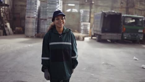 a-portrait-of-an-african-american-woman-in-a-special-green-uniform-is-walking-in-a-waste-processing-plant.-Factory-background.-Processing-of-raw-materials,-recycling.-Pollution-control
