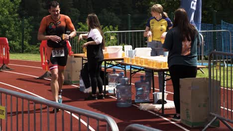 Runner-pouring-cup-of-cold-water-over-his-head-at-triathlon-check-point
