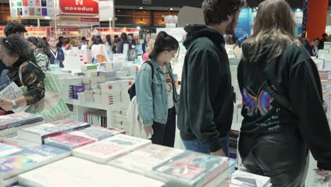 Couple-in-black-clothes-walk-up-towards-tall-stack-of-books-at-bookfair