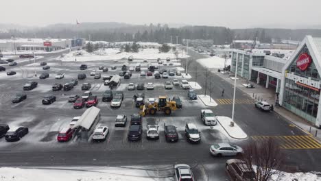 Aerial-of-CAT-snow-pusher-clearing-winter-snow-in-mall-parking-lot