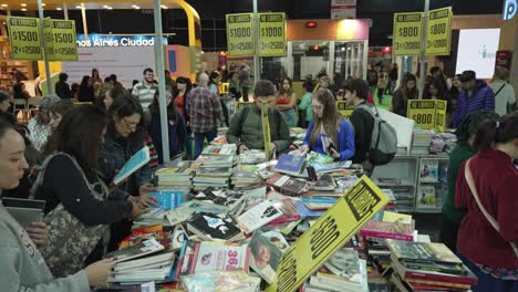 Descending-shot-above-messy-busy-book-table-at-fair-with-crowds-of-people-walking-by