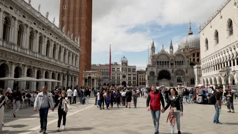 A-busy-day-on-the-Piazza-San-Marco-as-people-walk-through-the-square-surrounded-by-the-beautiful-buildings-and-architecture-of-the-historical-city,-Venice,-Italy