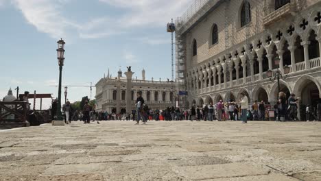 Tourists-Walking-Along-Pier-Beside-Doge's-Palace-With-Biblioteca-Nazionale-Marciana-In-background-In-Venice-On-Sunny-Day