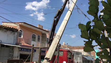 Construction-workers-lifting-damaged-concrete-utility-pylon-next-to-power-lines