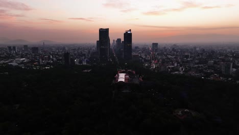Drone-shot-circling-silhouette-skyscrapers-of-downtown-Mexico-city,-colorful-evening