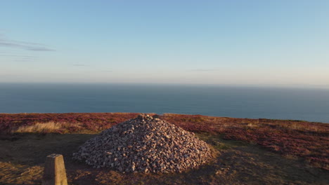 Stone-Cairn-at-Sunrise-on-Cliff-Above-the-Ocean-Sea---Pushing-Drone-Shot-4K-UHD