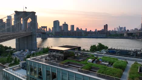 Luftaufnahme-Eines-Paares,-Das-Im-Café-Auf-Dem-Dach-Sitzt-Und-Den-Blick-Auf-Die-Skyline-Von-New-York-Und-Die-Brooklyn-Bridge-Sowie-Den-Sonnenuntergang-Genießt-–-Panorama-Weitwinkelaufnahme