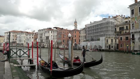 Eine-Filmische-Ansicht-Eines-Bootsmanns,-Der-Mit-Seinem-Boot-Auf-Dem-Canal-Grande-In-Venedig-Fährt,-Mit-Bunten-Gebäuden-Und-Wolken-Im-Hintergrund