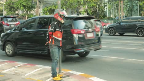 Motorbike-Taxi-Driver-Standing-Against-Post-on-the-Sidewalk-of-Bangkok,-Thailand