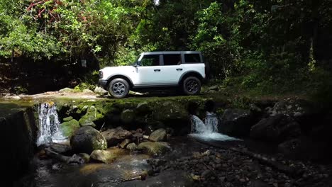 driving-ford-bronco-on-ballast-in-the-forest,-over-a-river