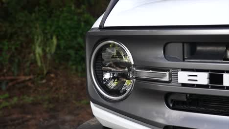 driving-ford-bronco-on-ballast-in-the-forest,-automotive-grill,-CAR-LIGHTS