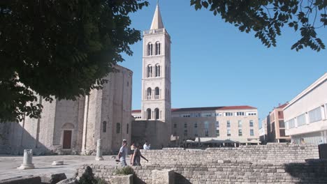 Pedestrians-walking-among-stone-archaeological-ruins-and-white-stone-church-of-the-st