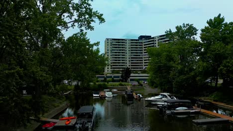 4k60-drone-reveal-behind-trees-overlooking-public-boat-tours-for-the-community-of-Laval-Quebec-South-Shore-with-rental-boats-kayaks-tours-and-nobody-outside-on-flat-water-partly-cloudy