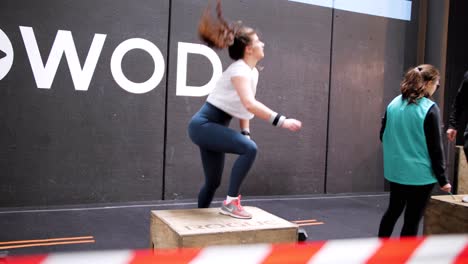Dynamic-CrossFit-Competition:-Ponytailed-Girl-in-Blue-Leggings-Performing-Non-Stop-Jump-Box-Jumps,-Filmed-from-the-White-and-Red-Tape