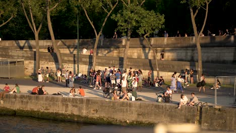 People-on-the-shore-of-the-Seine-river-enjoying-a-sunset-seen-from-river-boat,-Pan-left-shot
