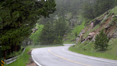 Cyclist-and-car-drive-in-pouring-rain-on-mountain-pass,-Boulder-countryside