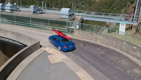 Tooma,-New-South-Wales,-Australia---27-December-2018:-Ford-car-with-kayak-on-roof-driving-along-the-Tooma-Dam-wall-in-the-Snowy-Mountains