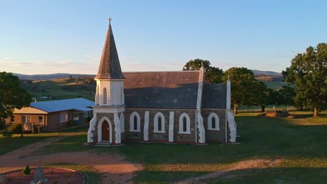 Adaminaby,-New-South-Wales,-Australia---30-December-2018:-Rising-over-the-Anglican-Church-in-Adaminaby-with-beautiful-afternoon-lit-hills-in-the-background