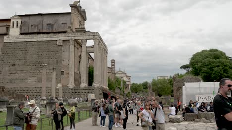 Tourists-Along-Via-Della-Salara-Vecchia-with-View-Of-Antoninus-and-Faustina-Temple-At-The-Roman-Forum-On-Overcast-Day