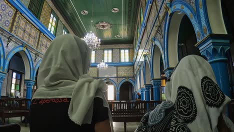 Back-view-of-adult-women-and-little-girl-with-headscarves-sitting-inside-El-Ghriba-Jewish-synagogue-of-Djerba-in-Tunisia