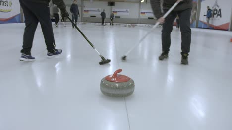 Following-curling-stone-with-two-players-sweeping-in-front-of-it