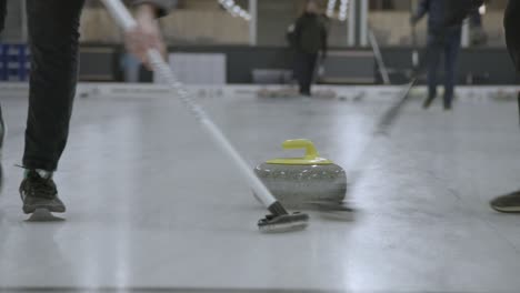 Two-players-swiping-the-ice-sheet-in-front-of-a-curling-stone