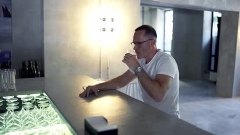 an-adult-man-in-glasses-sits-at-the-bar-counter-and-takes-a-sip-of-a-red-colored-cocktail