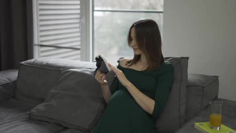 Glückliche-Frau,-Die-Zu-Hause-Auf-Dem-Sofa-Babyschuhe-Auf-Ihrem-Schwangeren-Bauch-Läuft