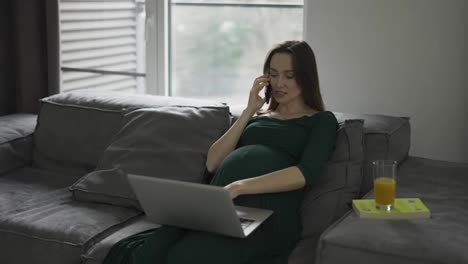 Pregnant-businesswoman-talking-mobile-phone-at-home-office-while-working-on-laptop