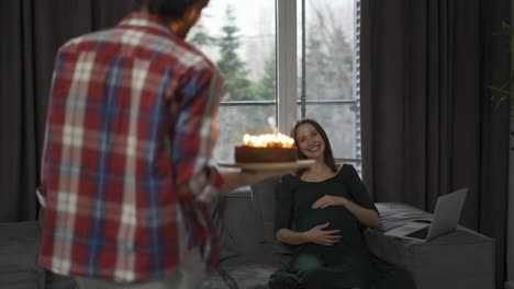 Ein-Mann-Mit-Geburtstagstorte-Und-Kerze-Schenkt-Sie-Einer-Schwangeren-Frau,-Die-Gemeinsam-Einen-Besonderen-Anlass-Feiert
