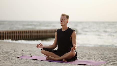 A-young-man-is-doing-yoga-and-meditating-on-a-sports-mat-while-sitting-during-the-dawn-of-the-sun.-Doing-a-specific-exercise.-Meditation,-hands.-Leisure-time,-recreation