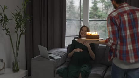 Ein-Mann-Mit-Geburtstagstorte-Und-Kerze,-Der-Sie-Einer-Schwangeren-Frau-Schenkt,-Die-Ihren-Geburtstag-Feiert
