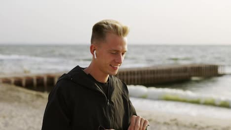 Portrait-of-a-young-man-who-listens-to-music-with-headphones-and-walks-along-the-beach-in-the-morning