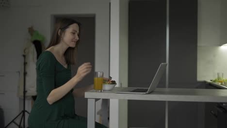 Pregnant-woman-sitting-and-eats-salad-while-having-a-video-call-on-laptop-at-home