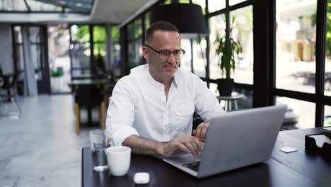 Smiling-businessman-working-on-laptop-computer-at-caffee.-Male-professional-typing-on-laptop-keyboard-at-caffee-workplace.-Portrait-of-positive-business-man-looking-at-laptop-screen-indoors