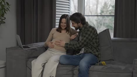 Pregnant-woman-with-large-belly-and-husband-sitting-on-sofa-in-loving-atmosphere