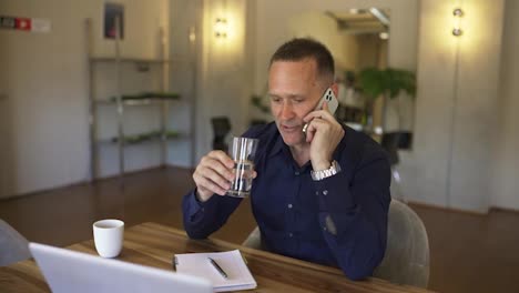 Happy-cheering-business-talking-over-the-phone.-Man-getting-great-news-on-the-phone-from-partners,-take-a-sip-from-water-glass