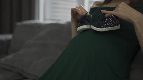 Mujer-Irreconocible-Caminando-Zapatos-De-Bebé-Sobre-Su-Vientre-Embarazado-En-Casa-En-El-Sofá