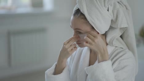 Woman-at-home-in-a-white-bathrobe-and-towel-applies-patches-under-the-eyes