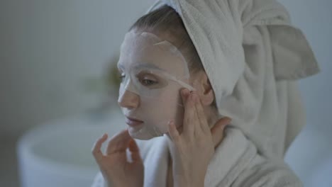 Nahaufnahme-Einer-Jungen-Hausfrau,-Die-Im-Badezimmer-Eine-Gewebe-Gesichtsmaske-Zur-Hautpflege-Aufträgt