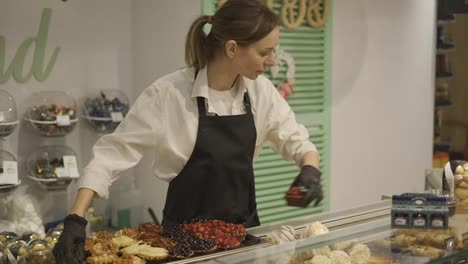 A-female-confectioner-in-a-black-apron-in-a-grocery-store-arranges-cakes-on-a-showcase