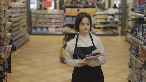 Girl-with-Down-syndrome-inspecting-shelves-with-goods-in-a-grocery-store-using-notebook