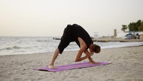 A-young-man-practices-yoga-while-standing-on-a-sports-mat-at-dawn.-Performing-a-specific-exercise.-Body-stretch.-Free-time,-rest