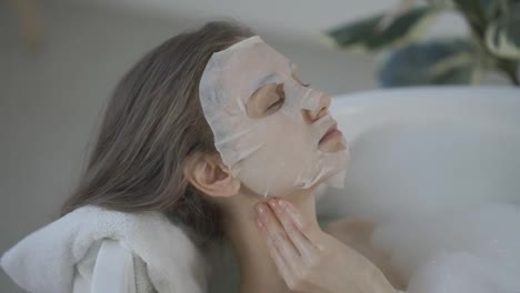 Junge-Frau-Mit-Gewebe-Gesichtsmaske-Zur-Hautpflege-Beim-Liegen-In-Der-Badewanne